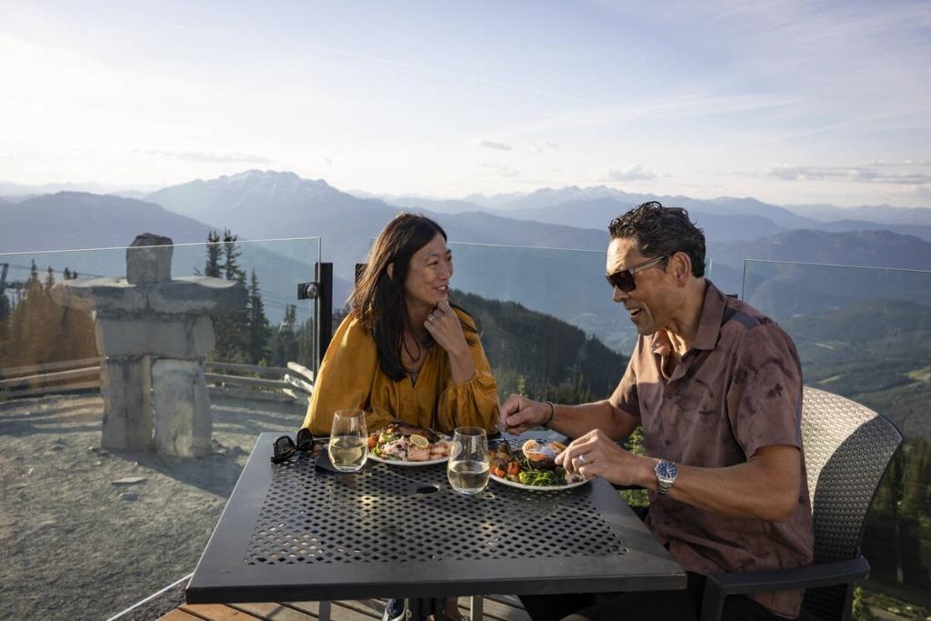 A couple dining on outdoor patio with panoramic mountain views at Whistler Blackcomb – scenic alpine restaurant experience
