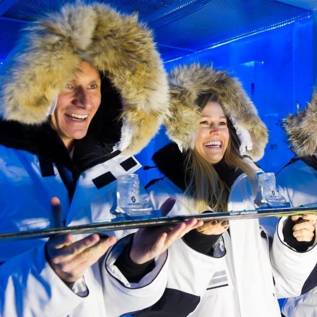 Guests wrapped in a thermal coat inside Whistler’s vodka ice room, surrounded by glowing ice walls and frosted shelves of chilled bottles.