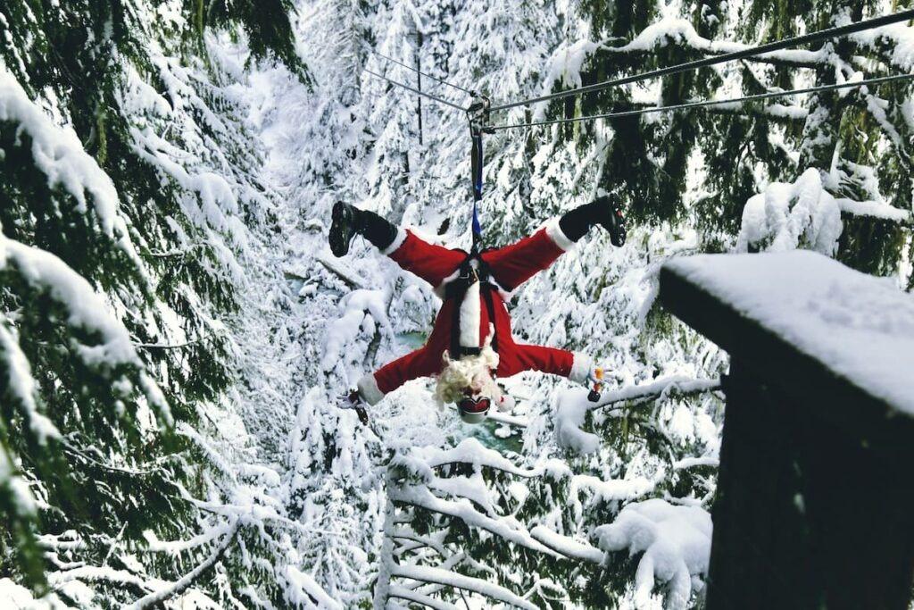 Santa ziplining upside down in Whistler surrounded by snow-covered trees