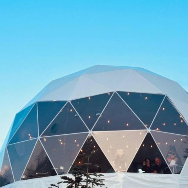Glass‑domed winter hideaway nestled in snow, warm interior glow with panoramic mountain views near Whistler.
