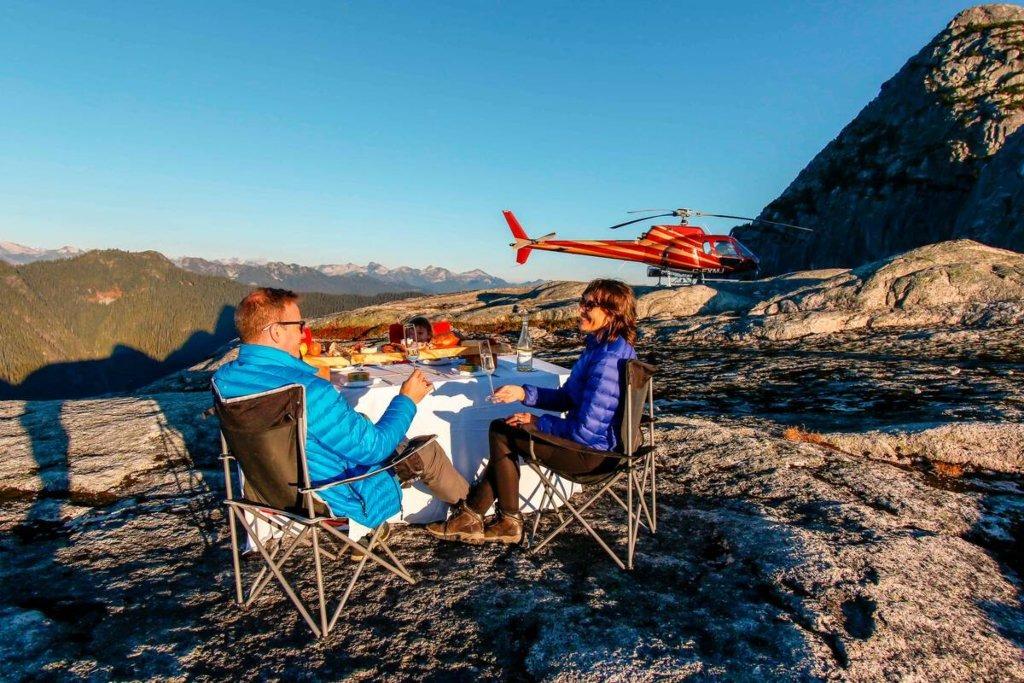 Luxury alpine picnic experience in Whistler, featuring a couple dining on a mountaintop after a helicopter ride with panoramic mountain views.